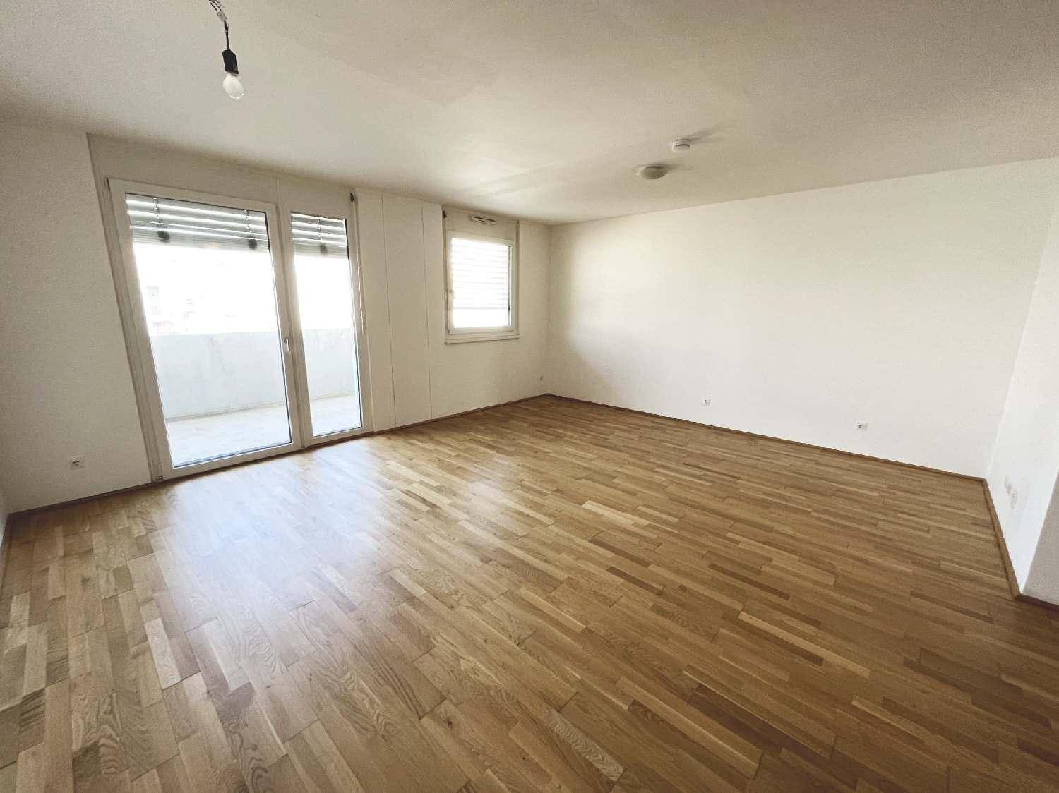 Geräumiges Wohnzimmer mit hellem Parkettboden und großen Fenstern zum Balkon.