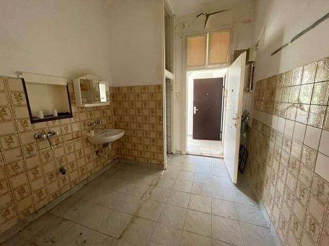 Gefliester Raum mit Waschbecken und Spuren früherer Nutzung, in renovierungsbedürftigem Zustand.