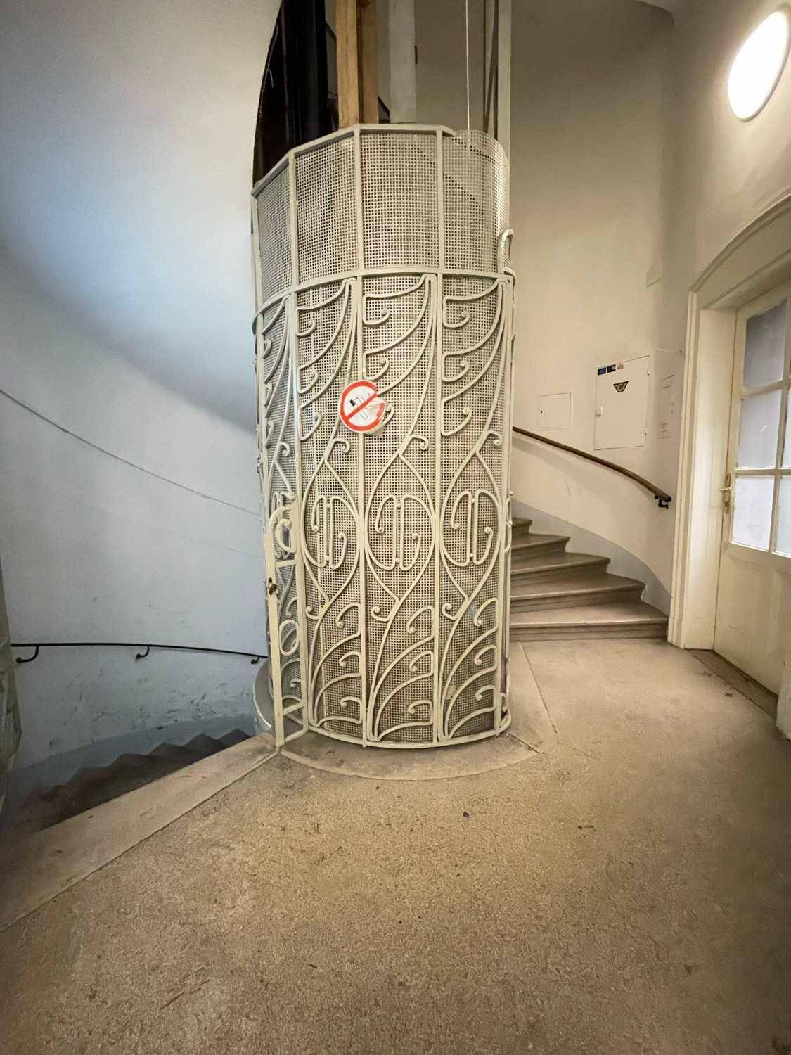 Historischer Aufzug mit kunstvollem Metallgitter in einem eleganten Treppenhaus eines Altbaus.
