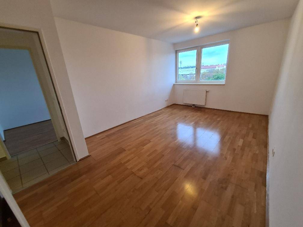 Geräumiges Schlafzimmer mit Holzboden und einem großen Fenster, das den Raum hell erscheinen lässt.