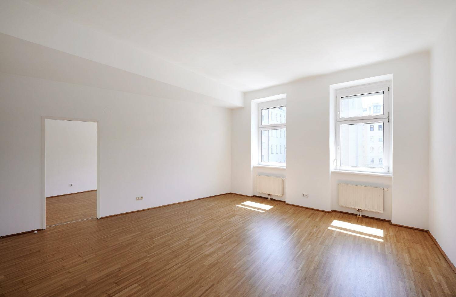 Geräumiges, helles Zimmer mit Parkettboden und zwei großen Fenstern, bereit zur Einrichtung.