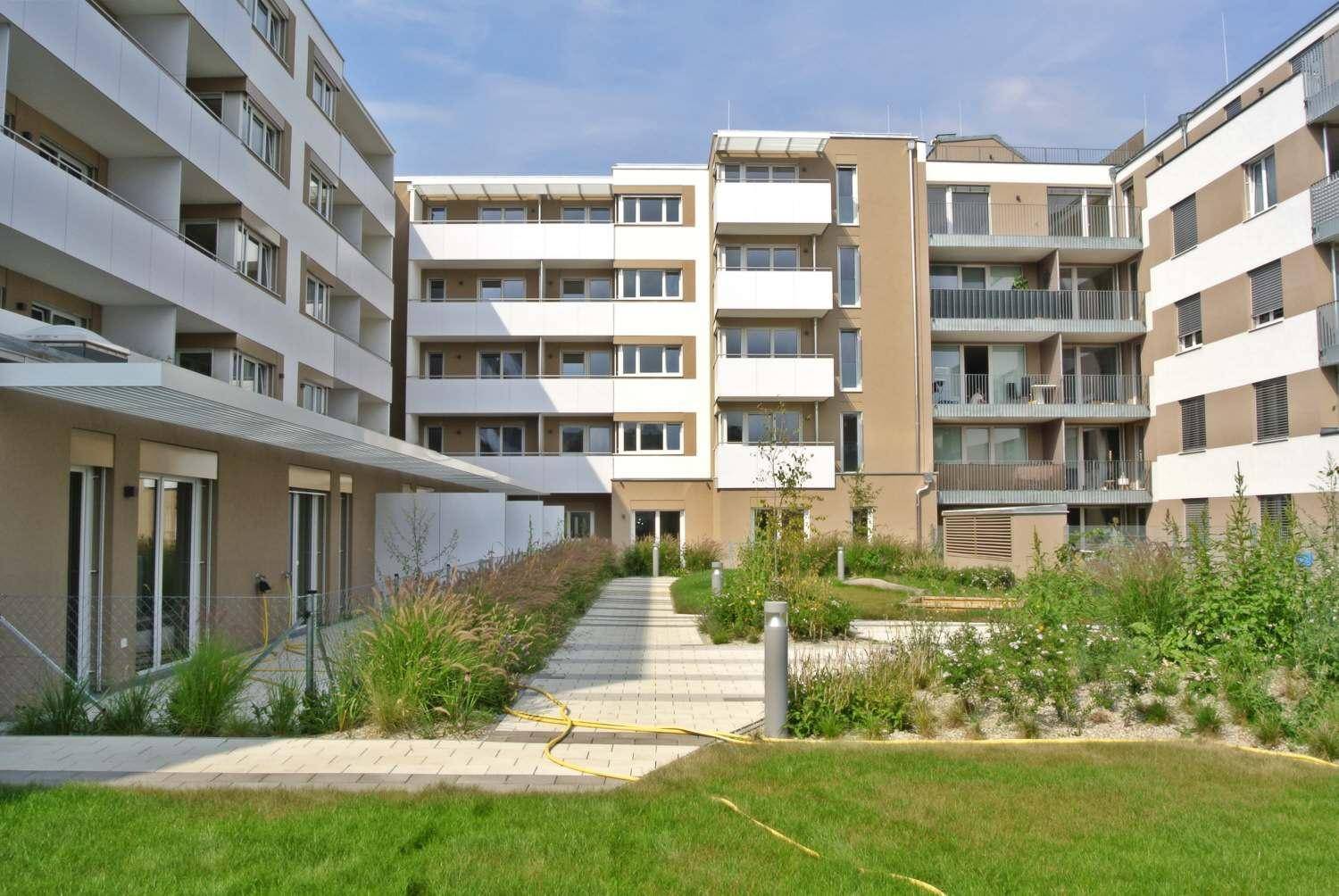 Gepflegter Innenhof mit Grünflächen, Gehwegen und modernen Wohngebäuden unter blauem Himmel.