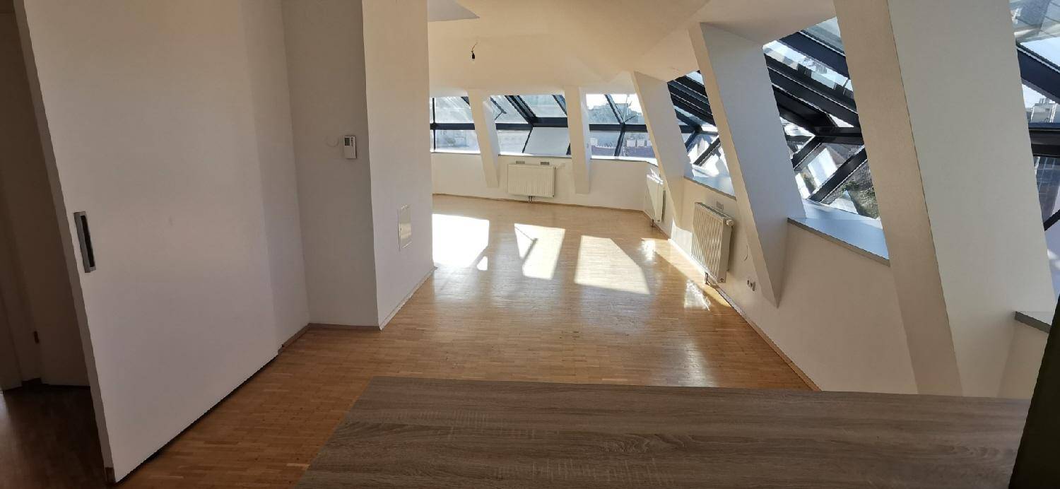 Geräumiger Wohnbereich mit Holzparkett und großen Fenstern, bietet viel Tageslicht und eine offene Atmosphäre.