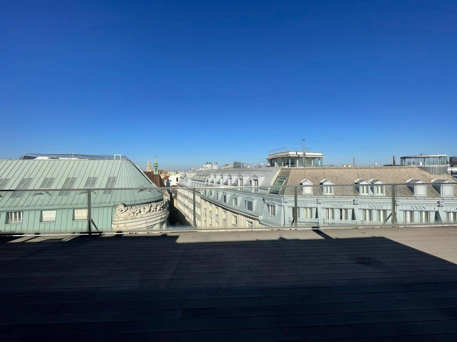 Weitläufiger Blick über die Dächer der Stadt von einer Dachterrasse unter klarem Himmel.