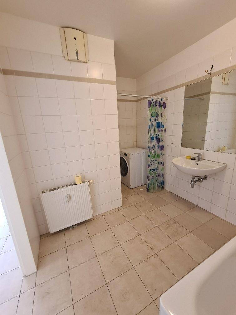 Gefliestes Badezimmer mit Waschbecken, Spiegel, Badewanne und Waschmaschine, hell und funktional.
