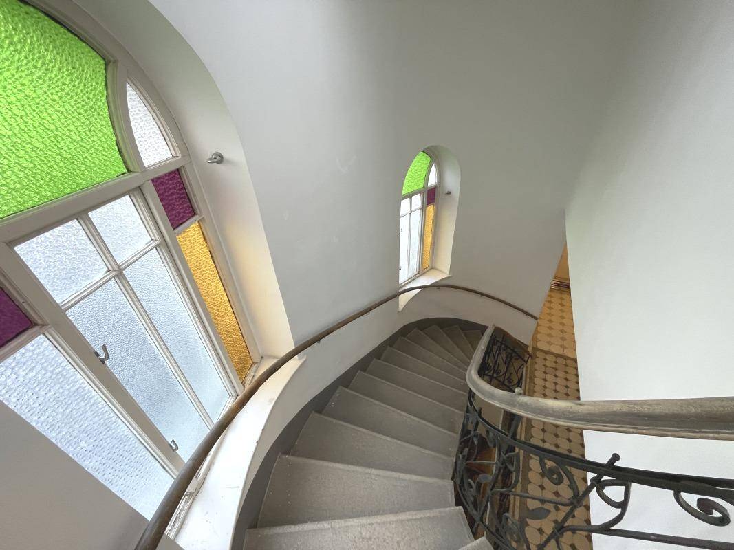 Wendeltreppe mit Buntglasfenstern und schmiedeeisernem Geländer in einem Altbau.