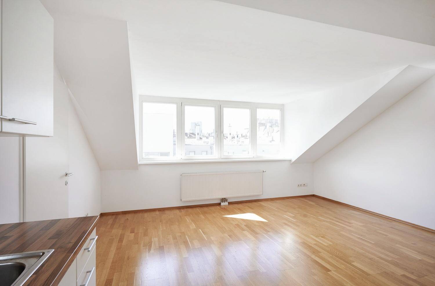Heller Raum im Dachgeschoss mit schrägen Wänden, großen Fenstern und Parkettboden.