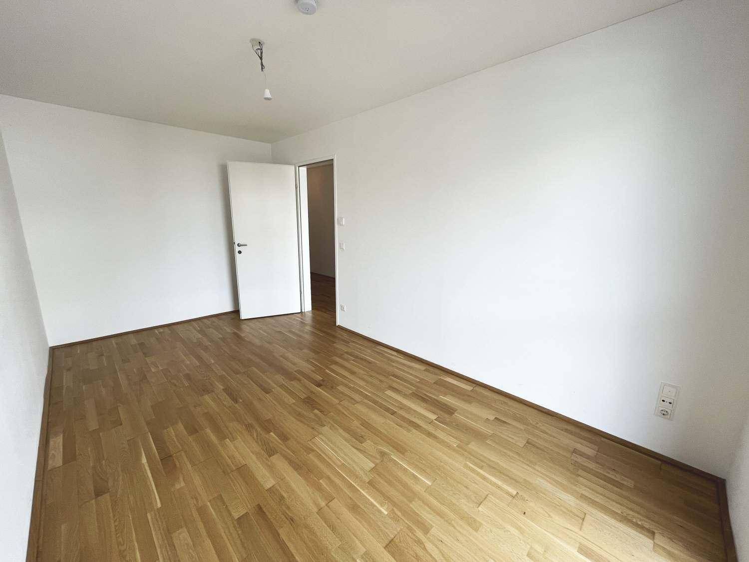 Leeres, helles Zimmer mit neuem Parkettboden und frisch gestrichenen weißen Wänden, bezugsfertig.