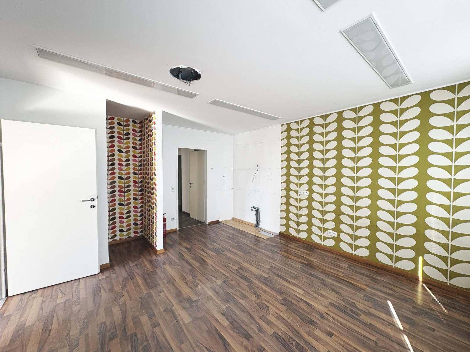 Leerer Raum mit Holzboden, einer auffälligen Tapetenwand und sichtbaren Kabeln an der Wand.