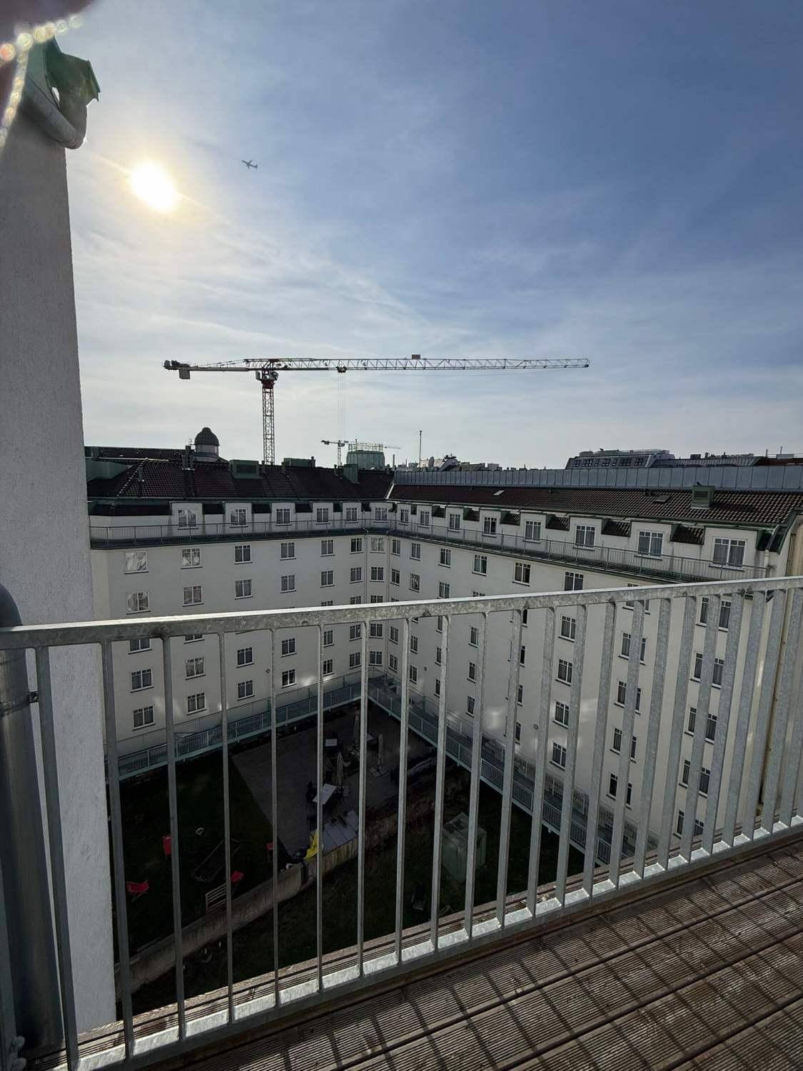 Balkon mit Blick auf einen ruhigen Innenhof und die umliegende Stadtlandschaft mit einem Kran.