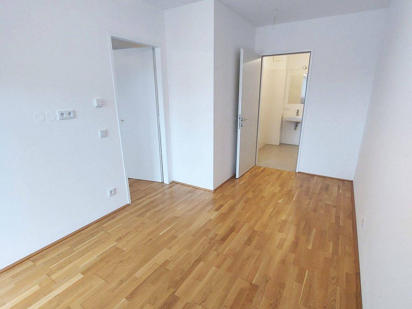 Heller Raum mit Parkettboden und Zugang zu einem Badezimmer.