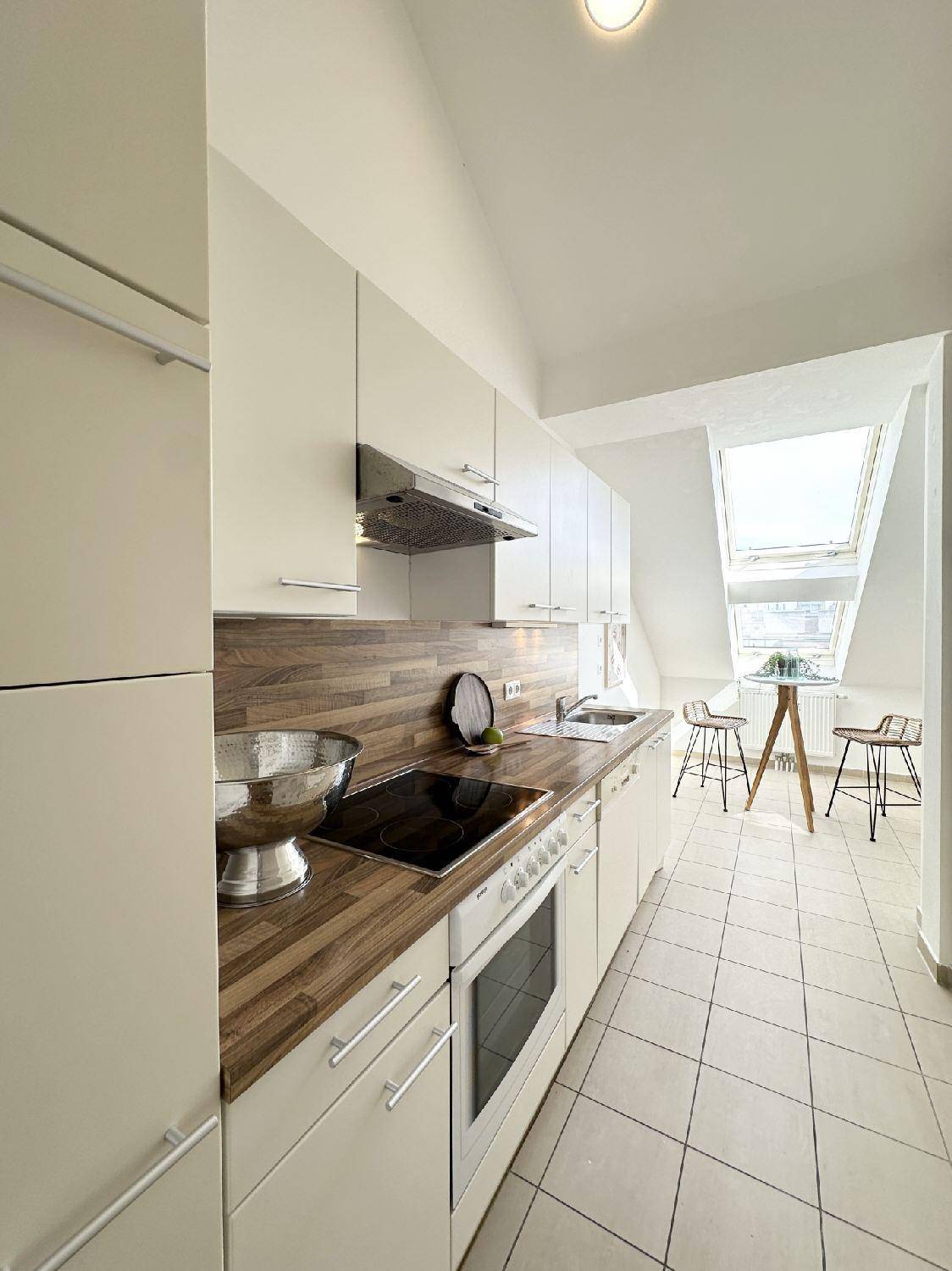 Moderne Küche mit weißen Schränken, Holzarbeitsplatte und Essbereich unter einem Dachfenster.