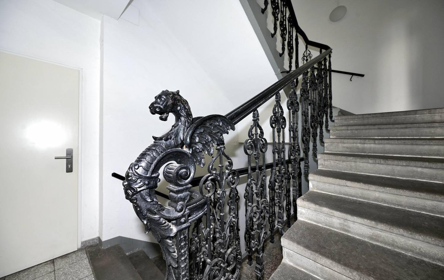 Historisches Treppenhaus mit kunstvollem schmiedeeisernem Geländer und Steinstufen.