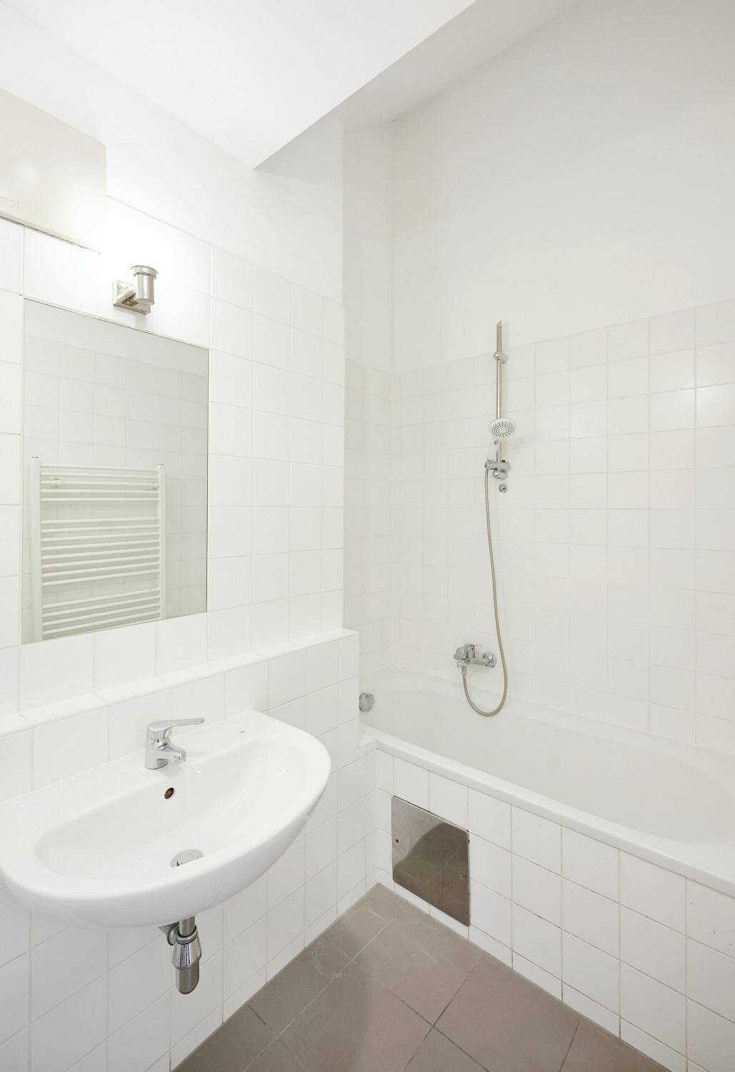 Helles Badezimmer mit Badewanne, Waschbecken, Spiegel und weiß gefliesten Wänden.
