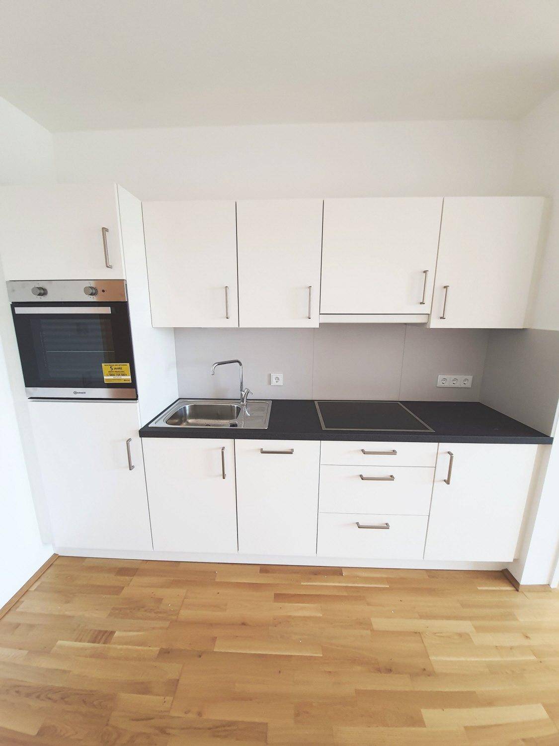 Moderne Küchenzeile mit weißen Schränken, dunkler Arbeitsplatte und integrierten Elektrogeräten.