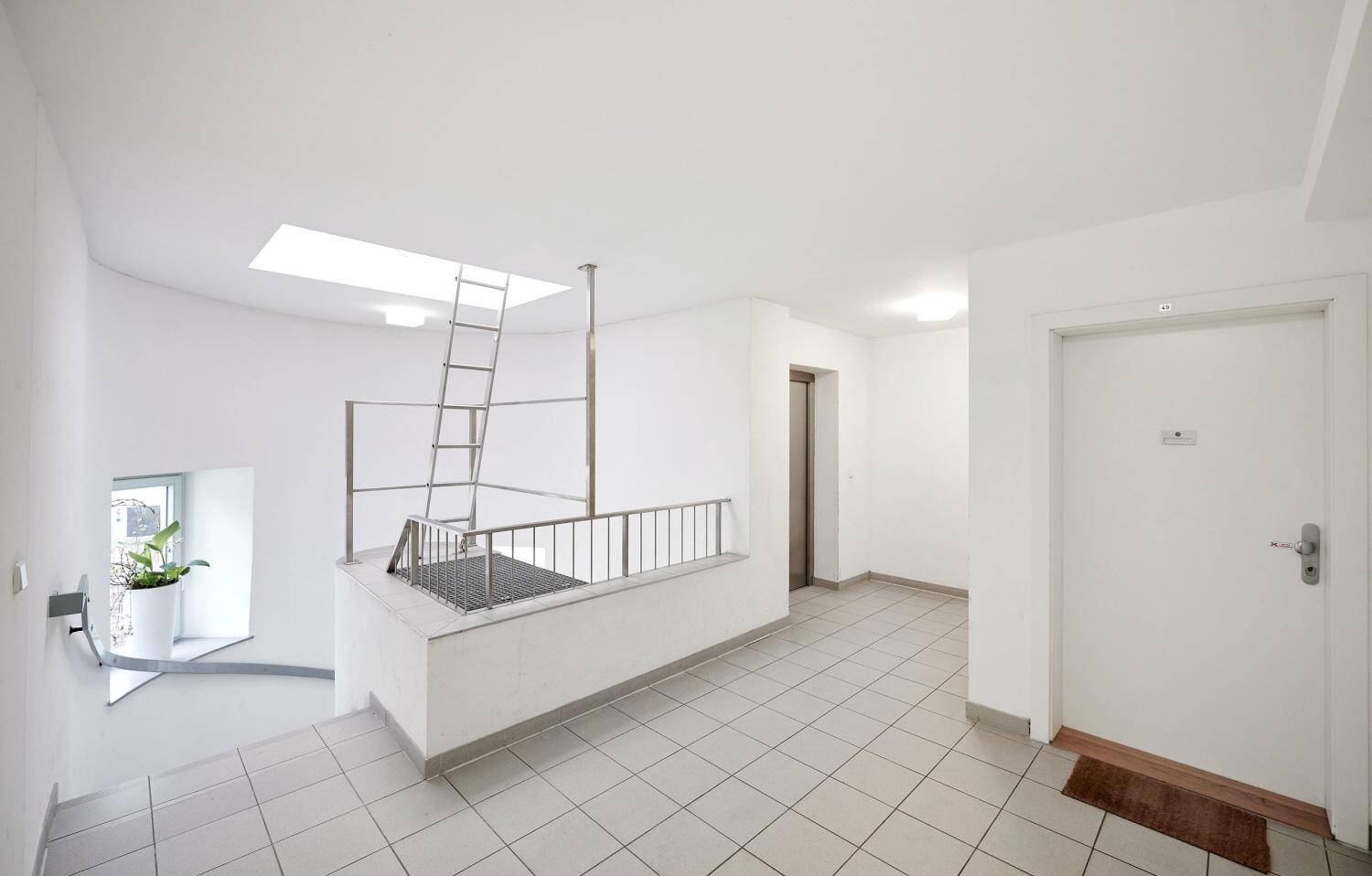 Heller Treppenabsatz mit Fliesenboden und einer Leiter, die zu einem Oberlicht führt.