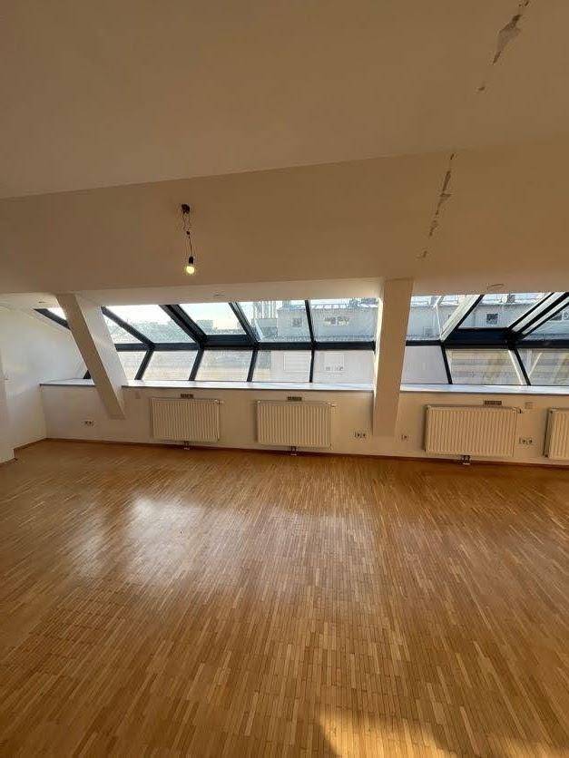 Geräumiger Dachgeschossraum mit Holzparkettboden und einer Reihe großer Dachfenster, die viel Licht spenden.