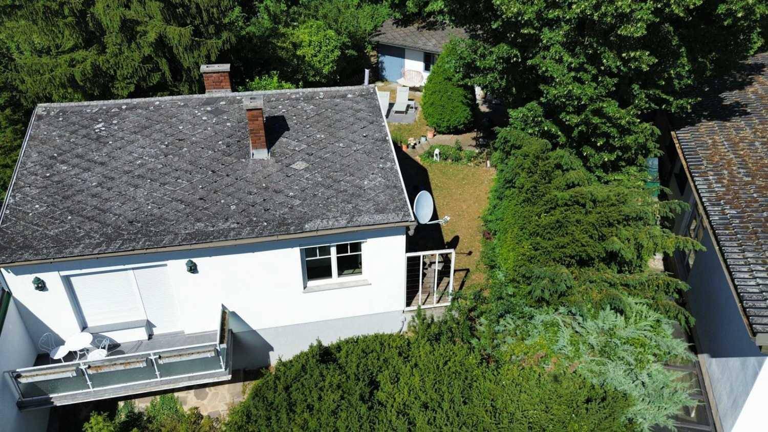 Luftaufnahme eines Hauses mit kleinem Balkon und Gartenbereich, umgeben von viel Grün.