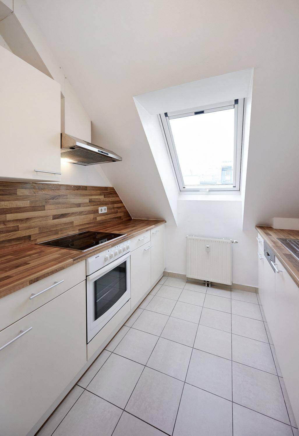 Helle Einbauküche mit weißen Fronten, Holzdetails, integriertem Backofen und einem Dachfenster.