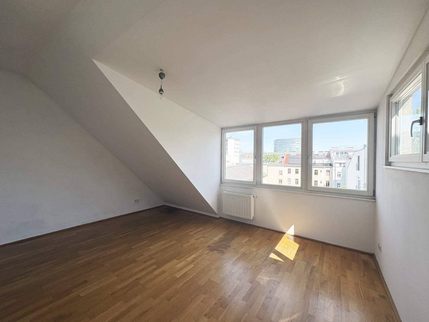 Geräumiges Zimmer mit Holzboden, Dachschräge und mehreren Fenstern mit Stadtblick.