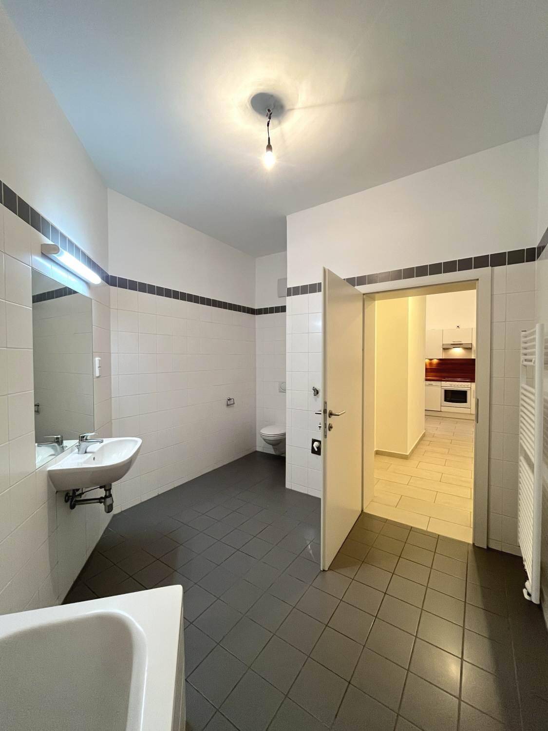 Badezimmer mit Waschbecken, Badewanne und Blick in den angrenzenden Raum.