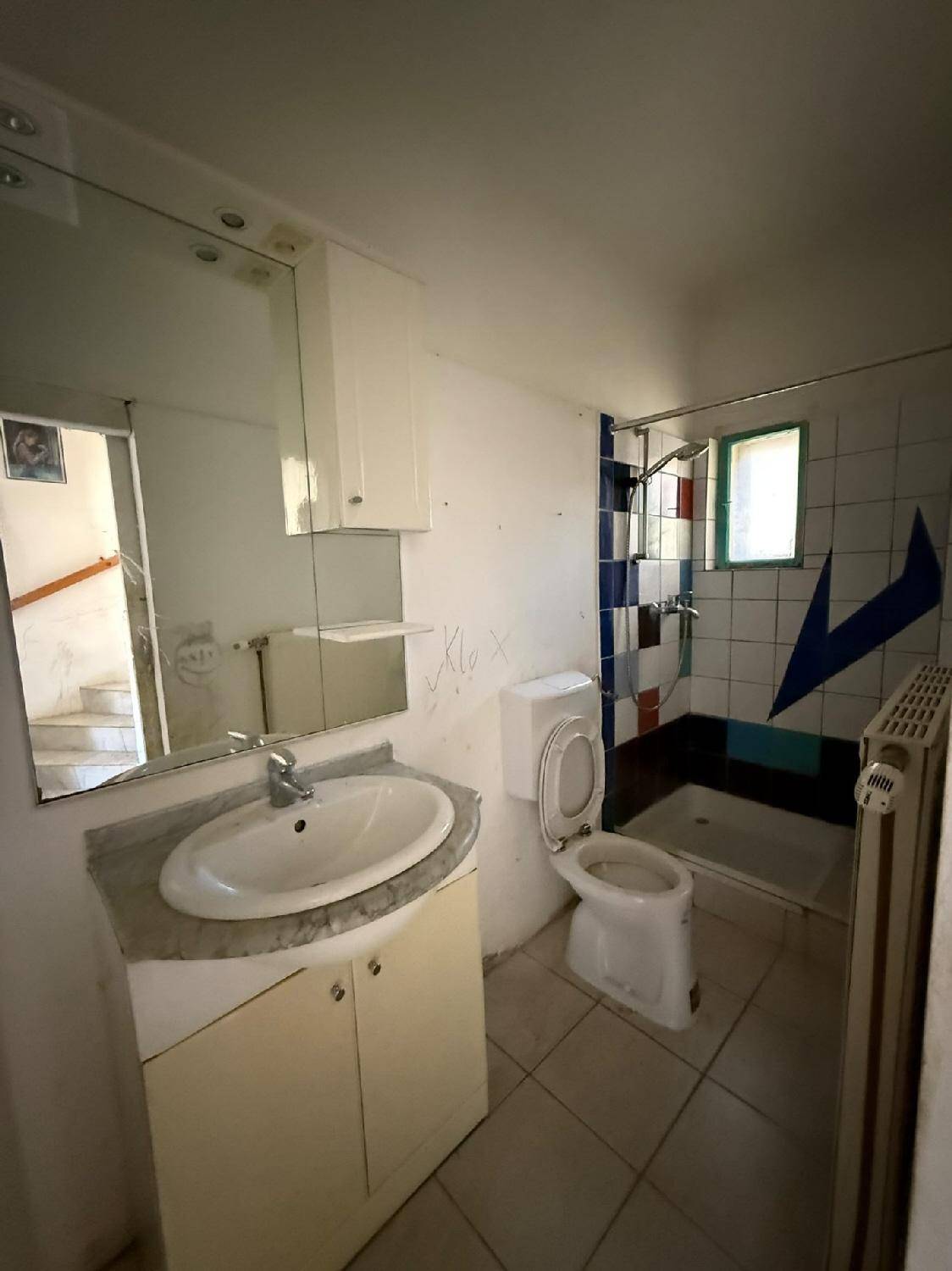 Badezimmer mit Waschbecken, Toilette und Duschbereich, gefliest und mit Fenster.