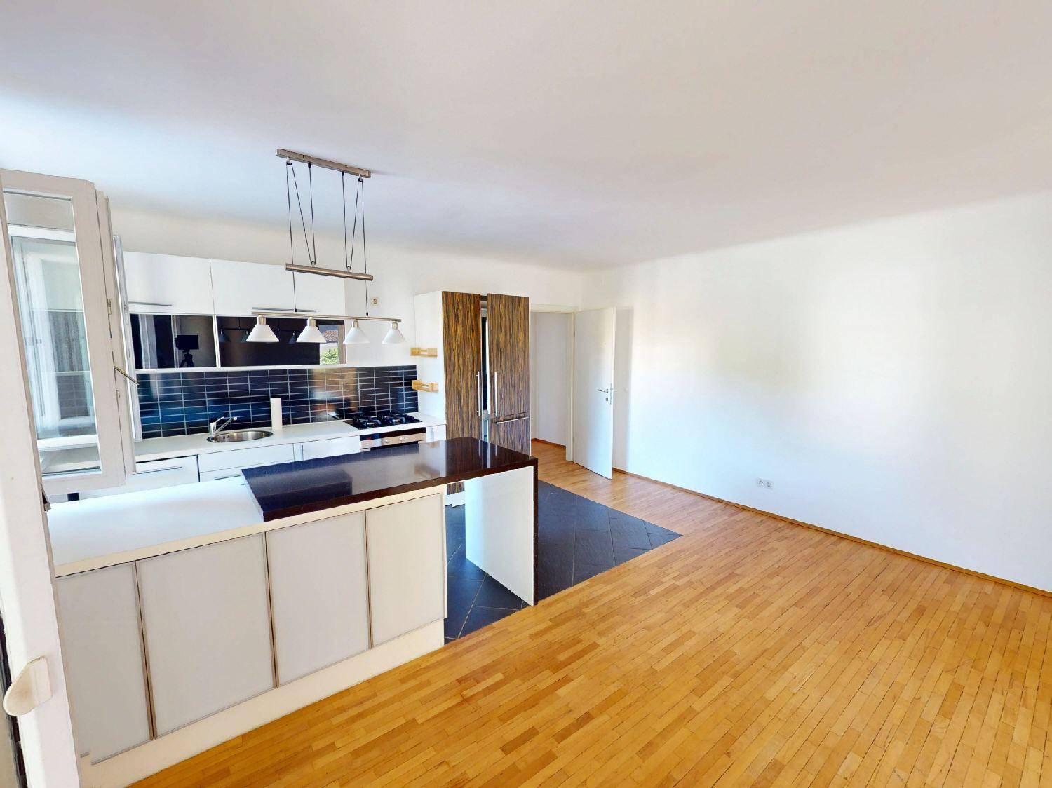 Moderne offene Küche mit dunkler Arbeitsplatte und integriertem Kühlschrank im Wohnbereich.
