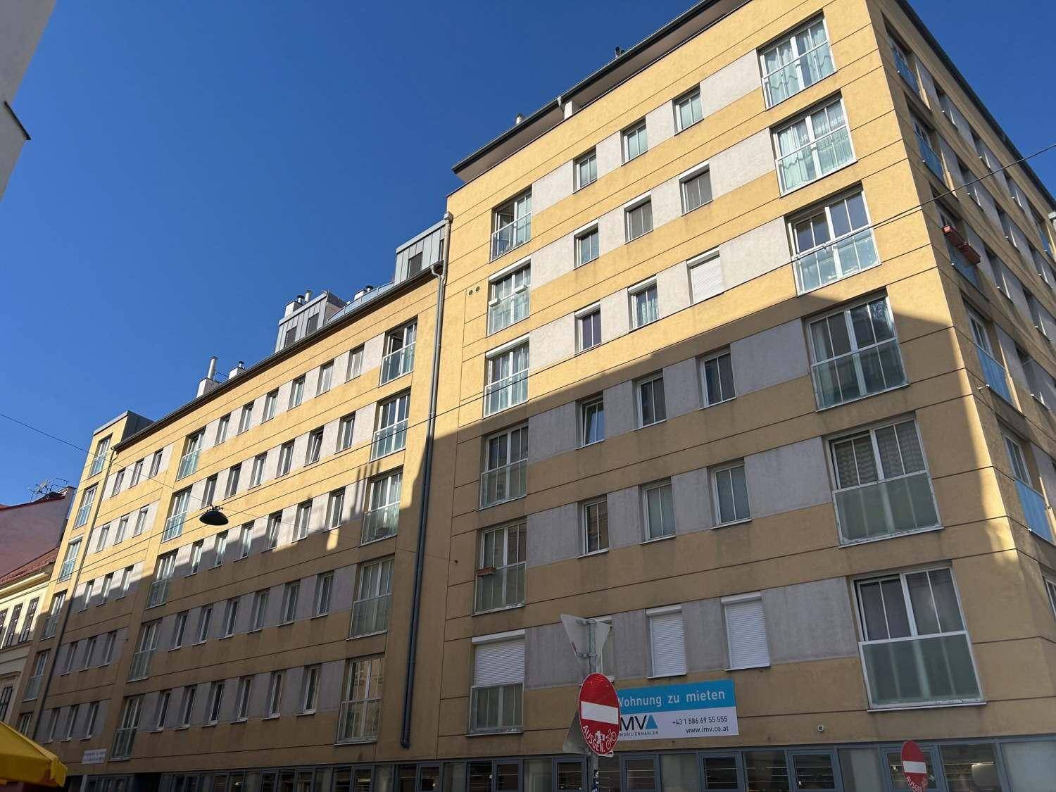 Seitenansicht des modernen Mehrfamilienhauses mit gelber Fassade unter blauem Himmel.