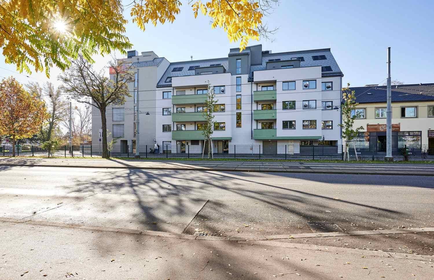 Moderne Wohnanlage mit grünen Akzenten und großen Fenstern an einer Straße gelegen.
