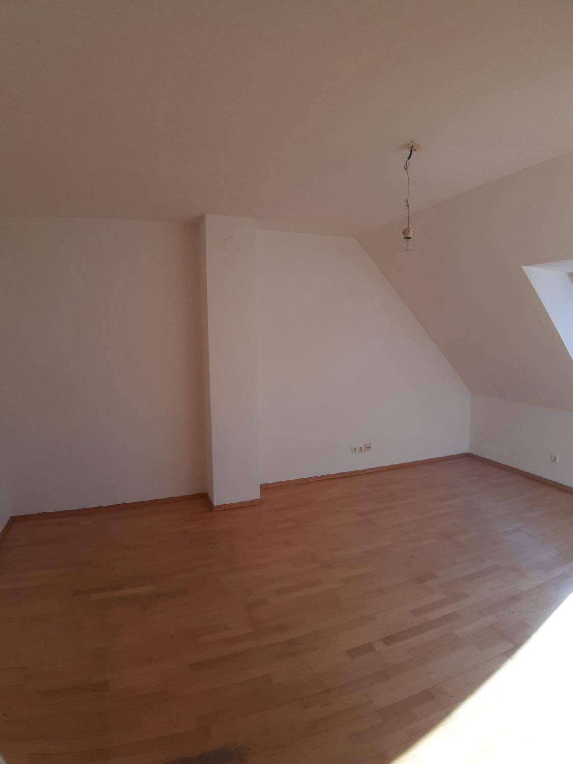 Leerer Dachgeschossraum mit hellem Holzboden und schrägen Wänden, bereit zur Einrichtung.