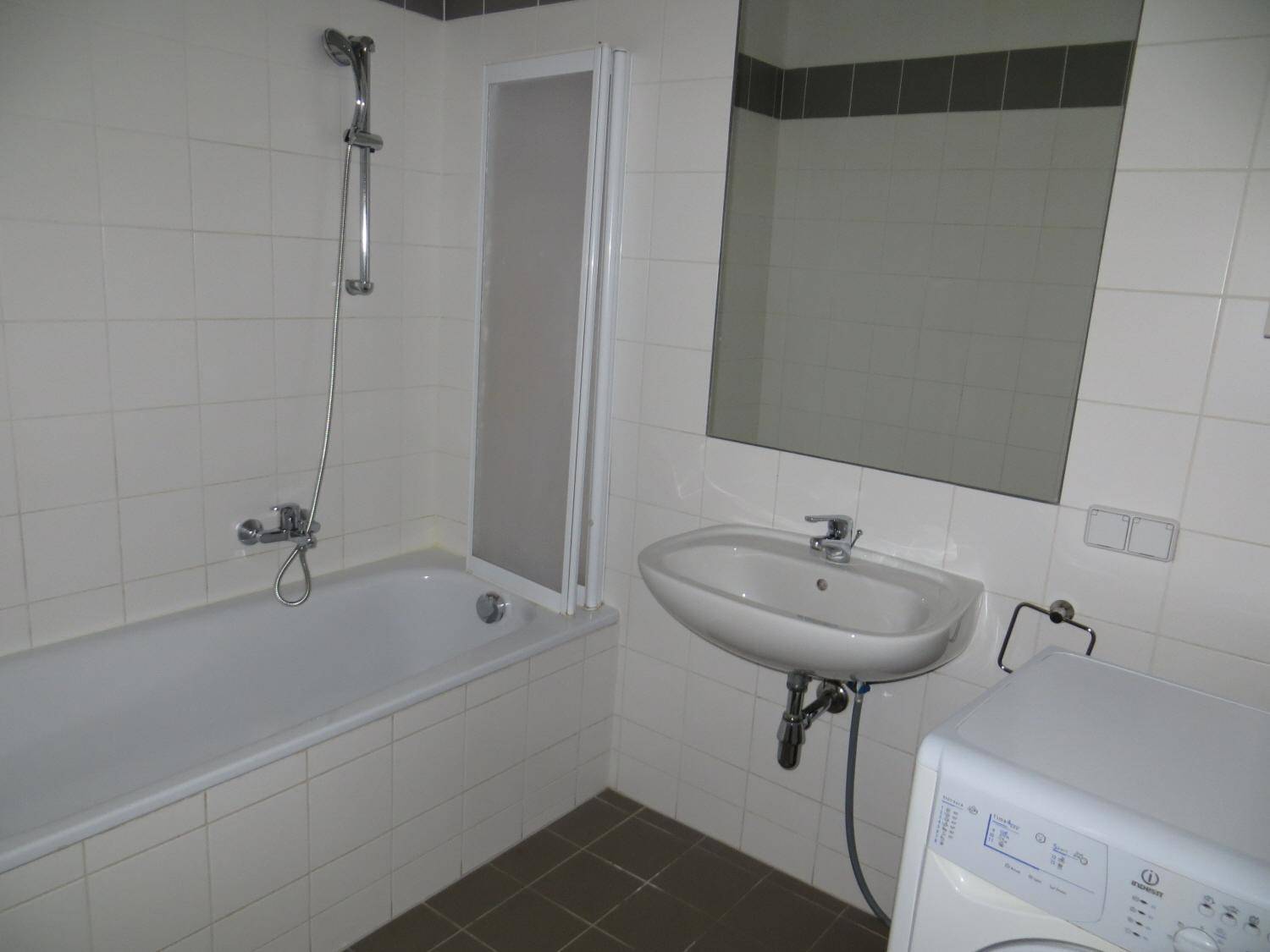 Funktionales Badezimmer mit Badewanne, Duschvorrichtung, Waschbecken und Waschmaschine, komplett gefliest.