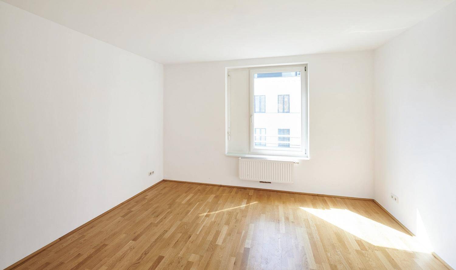 Helles Zimmer mit Parkettboden und einem Fenster, das viel natürliches Licht in den Raum bringt.
