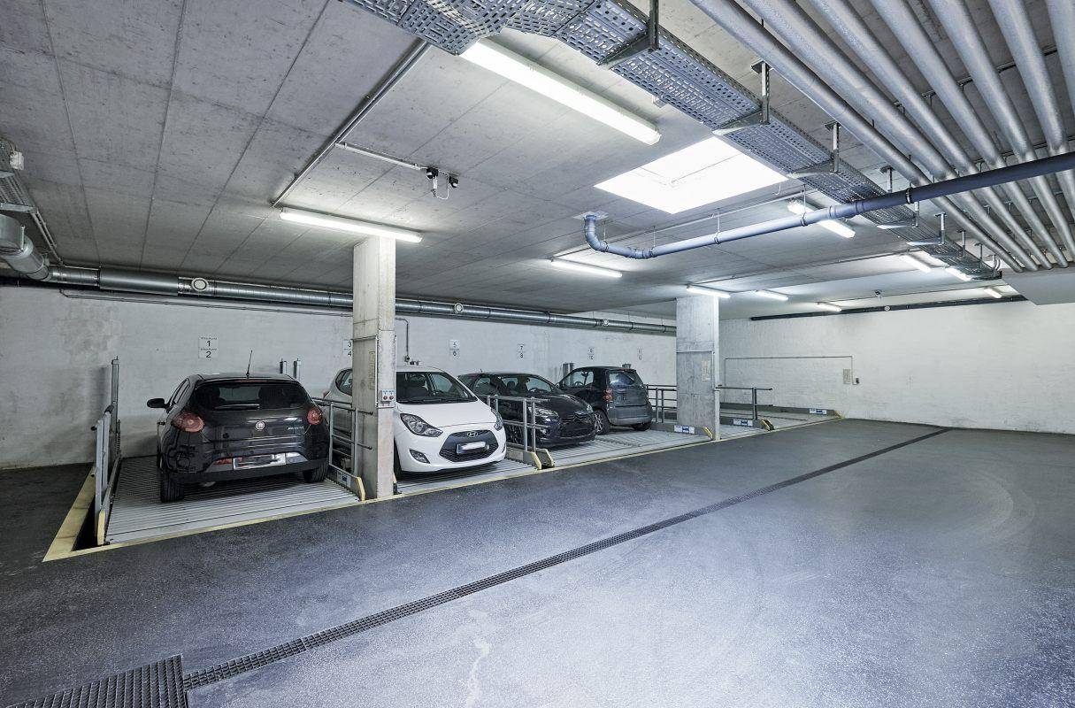 Helle Tiefgarage mit mehreren Parklifts und sichtbaren Installationen an der Decke.