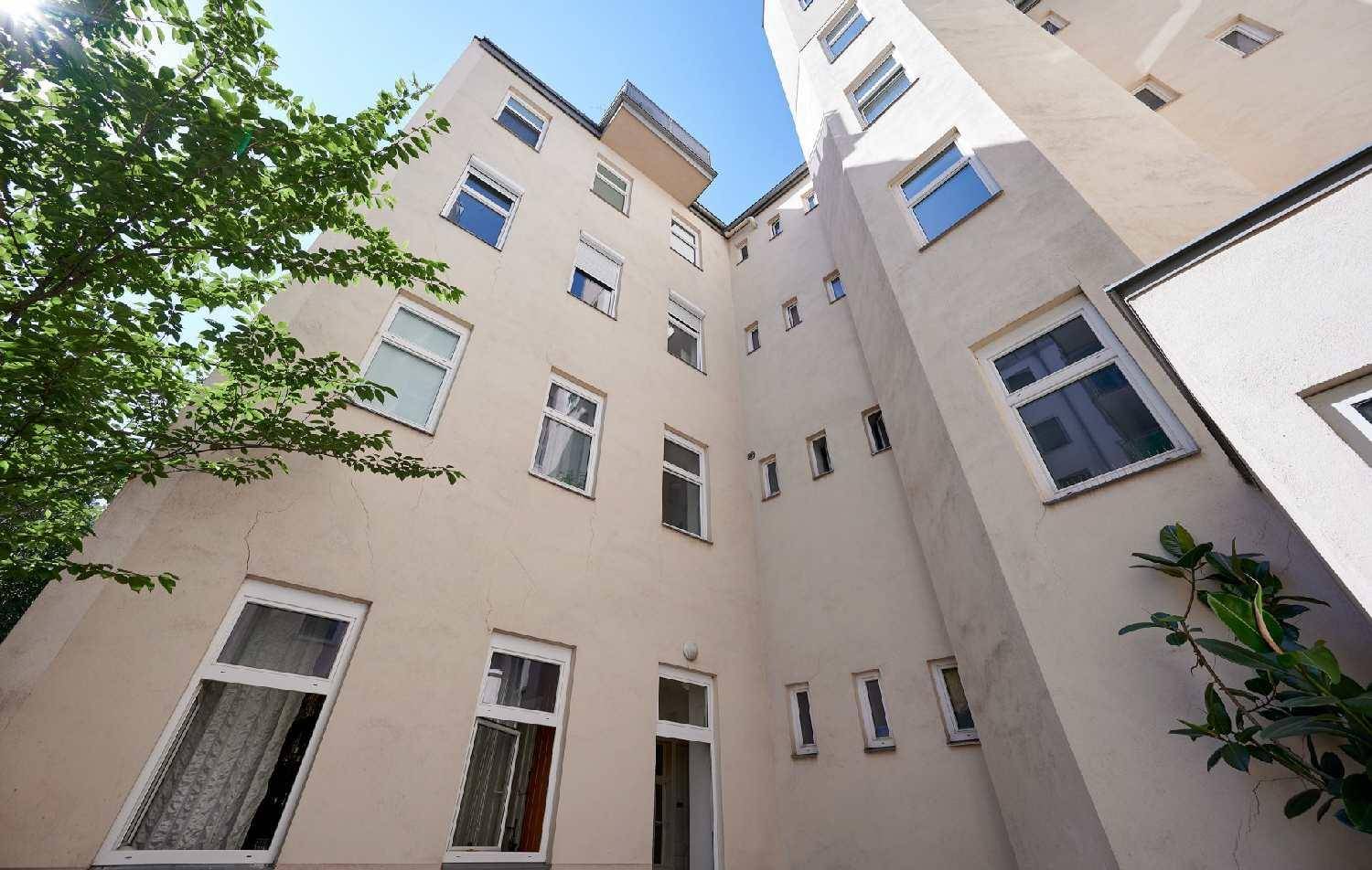 Blick nach oben in einen hellen Innenhof eines Wohngebäudes mit vielen Fenstern.