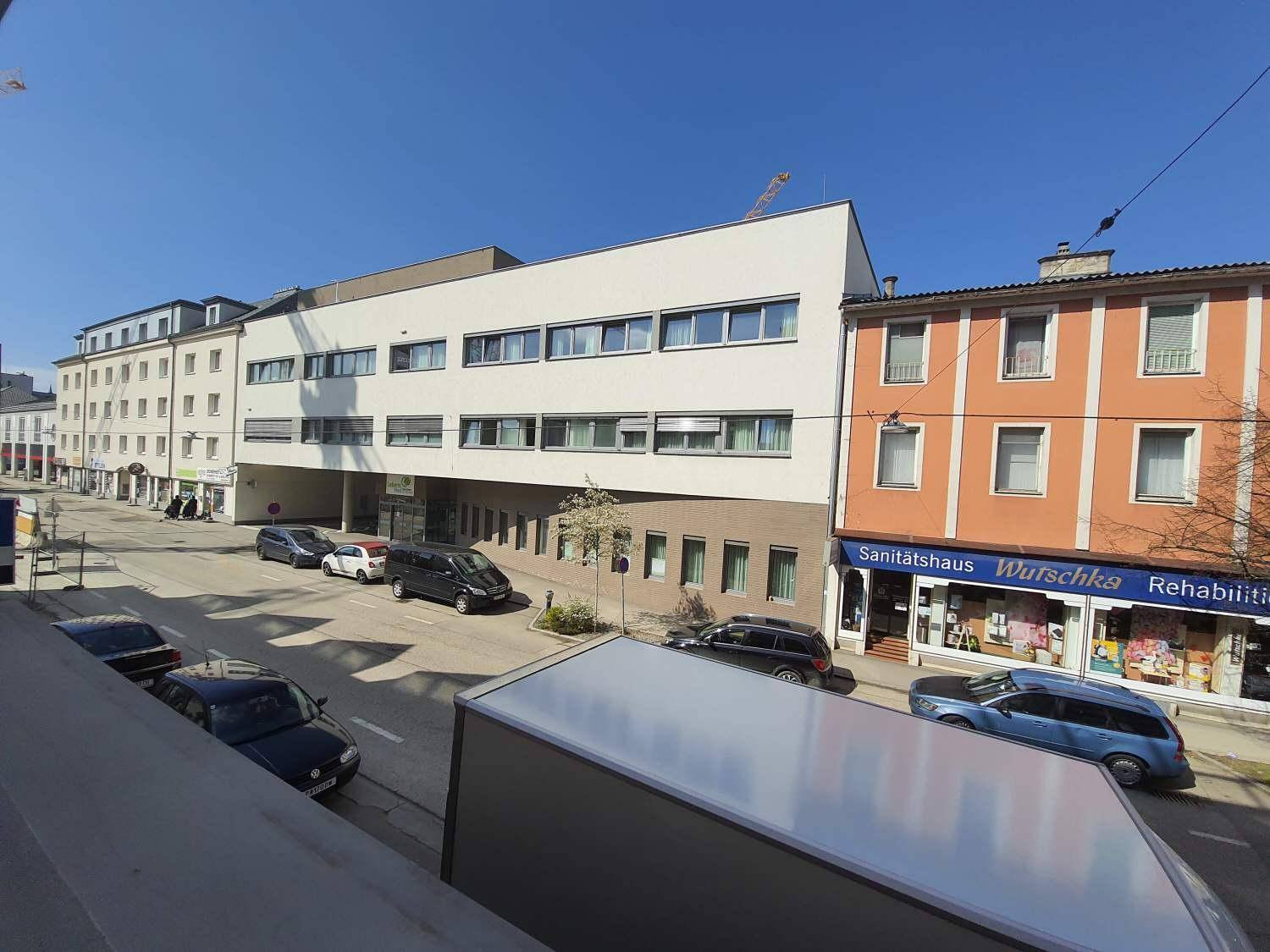Blick von einem Balkon auf die belebte Stadtstraße mit verschiedenen Gebäuden.