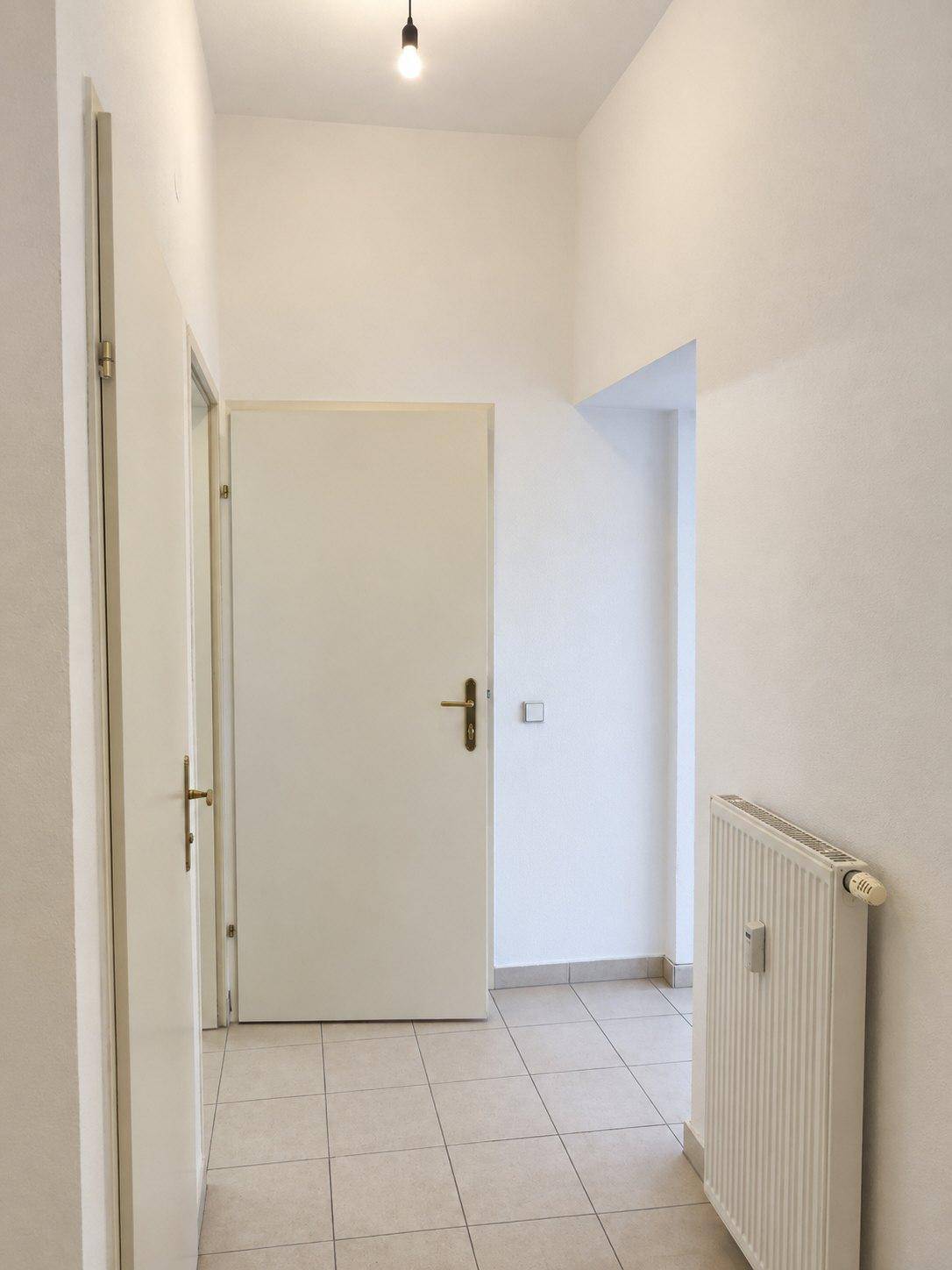 Heller Flur mit Fliesenboden und weißen Wänden, der zu verschiedenen Zimmern führt.