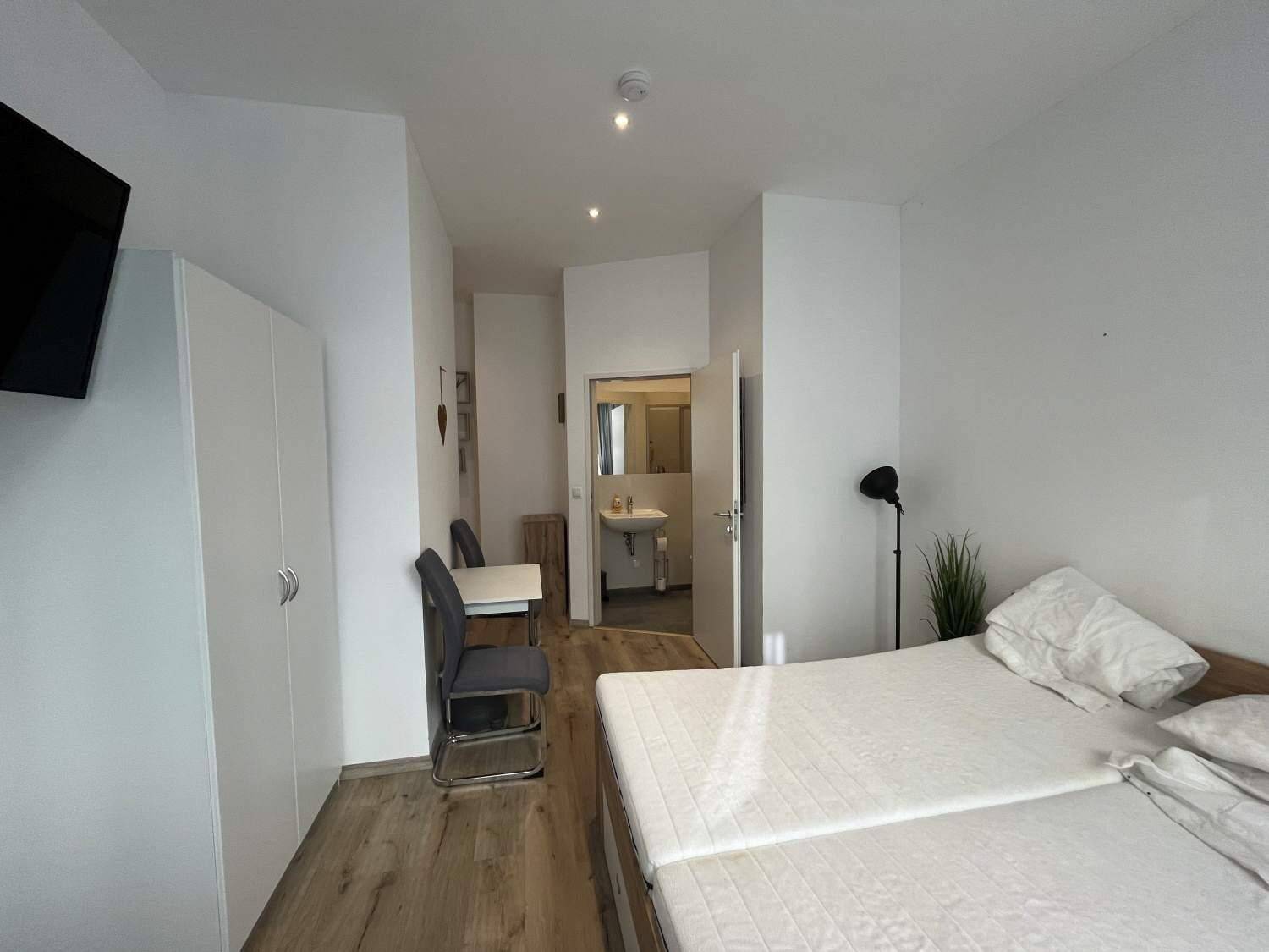 Geräumiges Schlafzimmer mit zwei Einzelbetten, weißem Kleiderschrank und Blick zum Badezimmer.