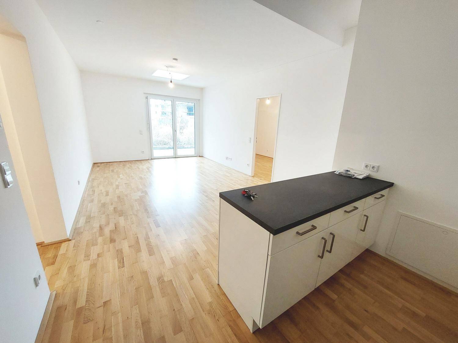 Heller, offener Wohnbereich mit Parkettboden, weiß gestrichenen Wänden und Zugang zu einer Terrasse.