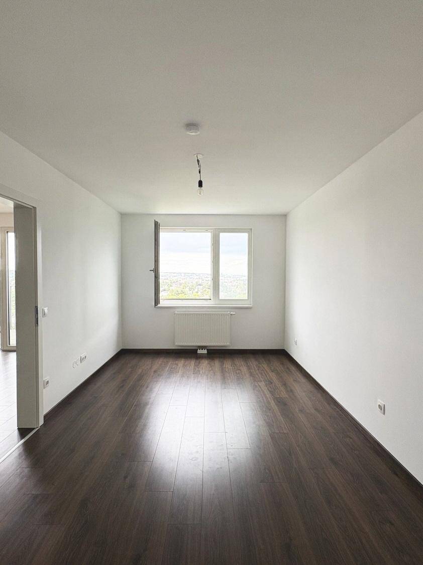 Helles Schlafzimmer mit dunklem Laminatboden, weißen Wänden und einem Fenster mit Weitblick.