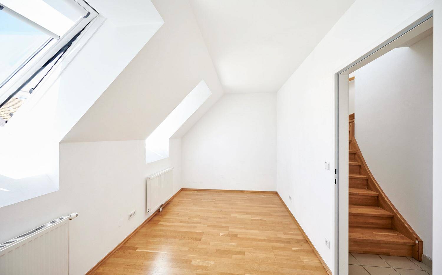 Helles Schlafzimmer im Dachgeschoss mit Holzboden und zwei Dachfenstern, bietet viel Licht.