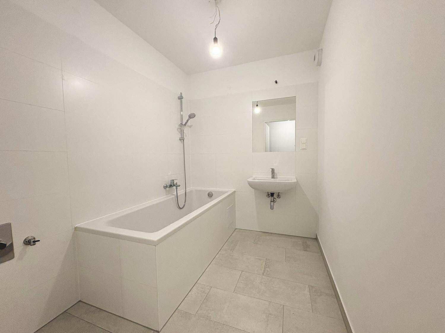Modernes Badezimmer mit Badewanne, Waschbecken und hellen Fliesen, funktional und sauber.