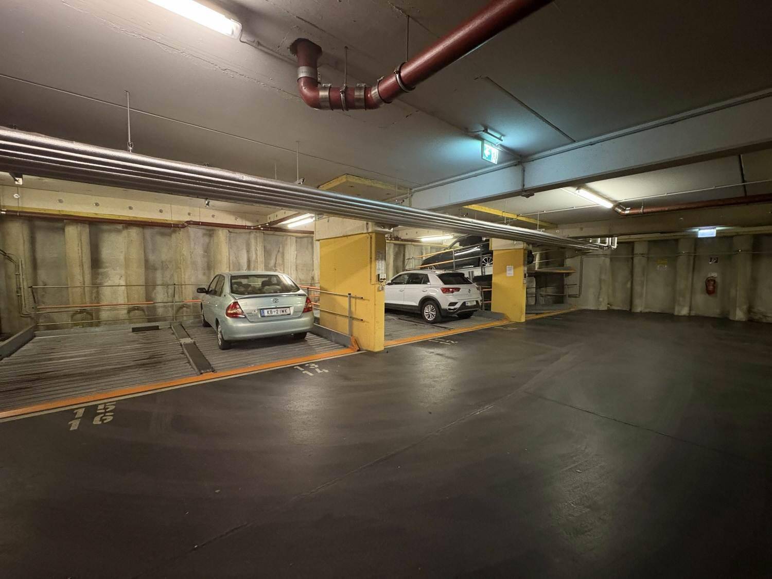 Geräumige Tiefgarage mit mehreren Parkplätzen und automatischen Hebebühnen für Fahrzeuge.