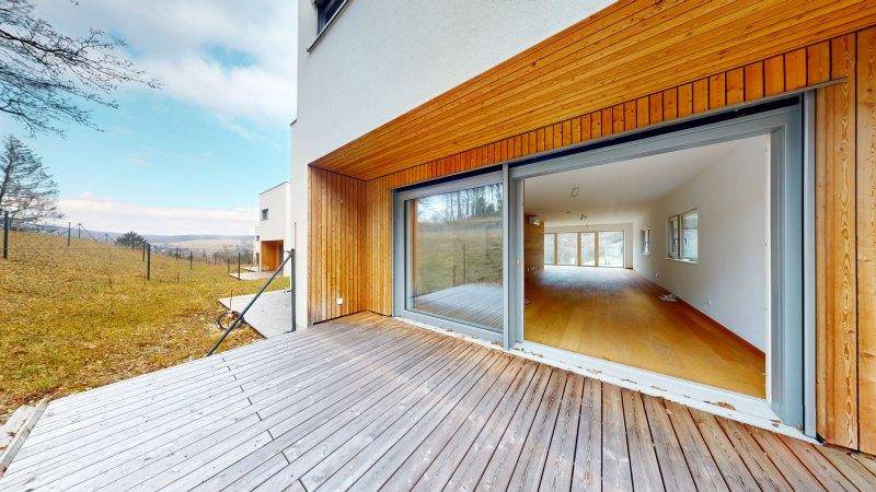 Große Holzterrasse mit Schiebetüren, die einen weiten Blick in die Landschaft bietet.