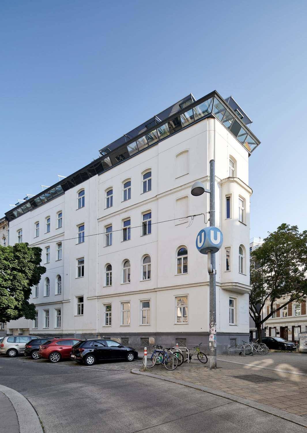 Eckgebäude mit moderner Dachaufstockung und Solarpaneelen in urbaner Umgebung.