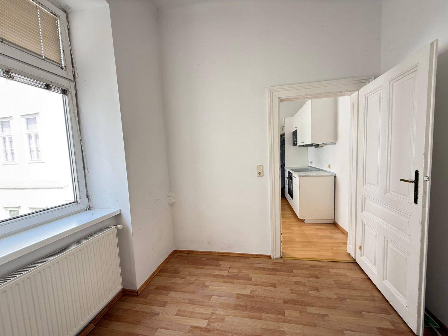 Helles Zimmer mit Holzboden und Fenster, das direkt zur Küche führt.
