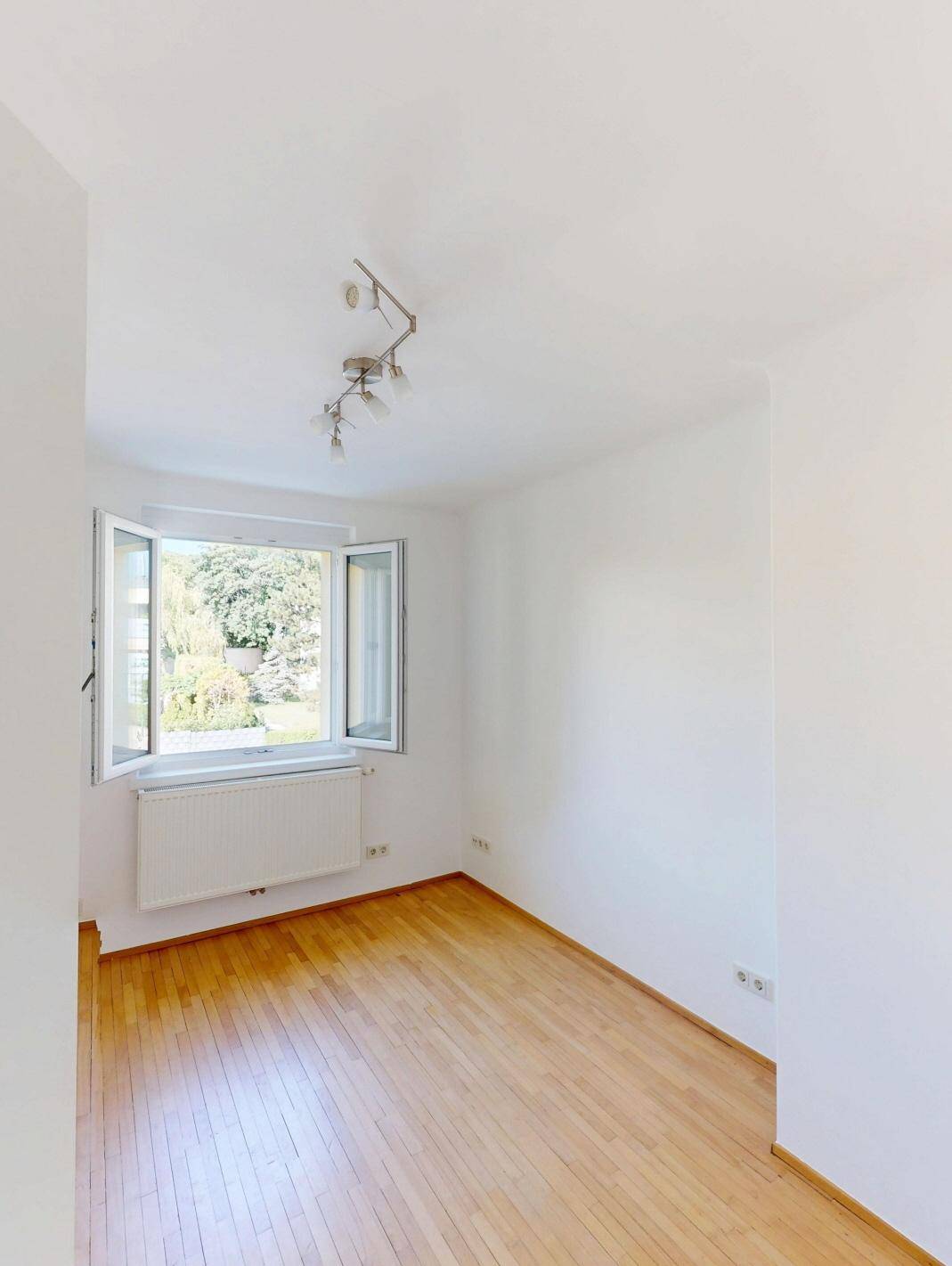 Freundliches Zimmer mit Parkettboden und großem Fenster, bietet viel Tageslicht.
