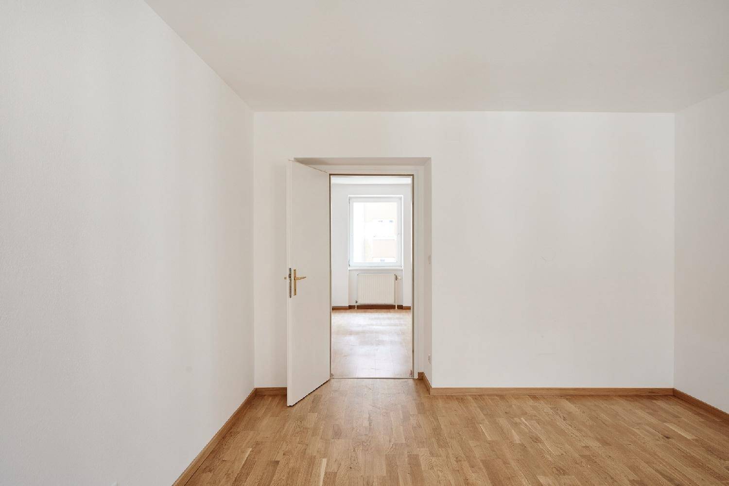 Heller Flur mit Parkettboden und offener Tür zu einem weiteren Zimmer.