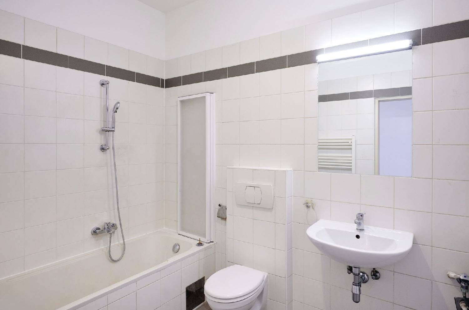 Funktionales Badezimmer mit weißen Fliesen, Badewanne mit Duschfunktion, WC und Waschbecken.