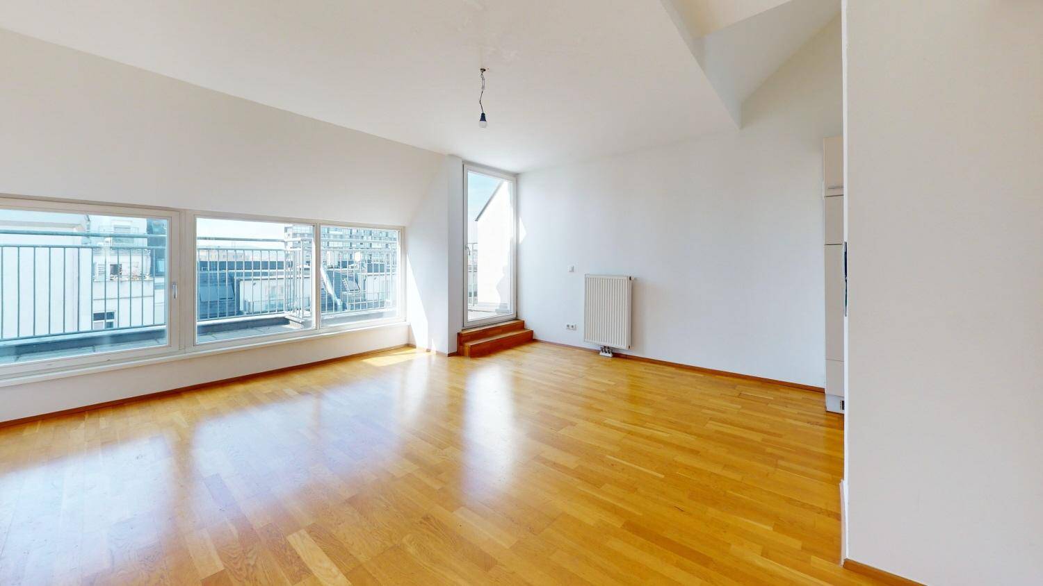 Geräumiger Wohnbereich mit Holzboden und großen Fenstern, die viel Tageslicht hereinlassen.