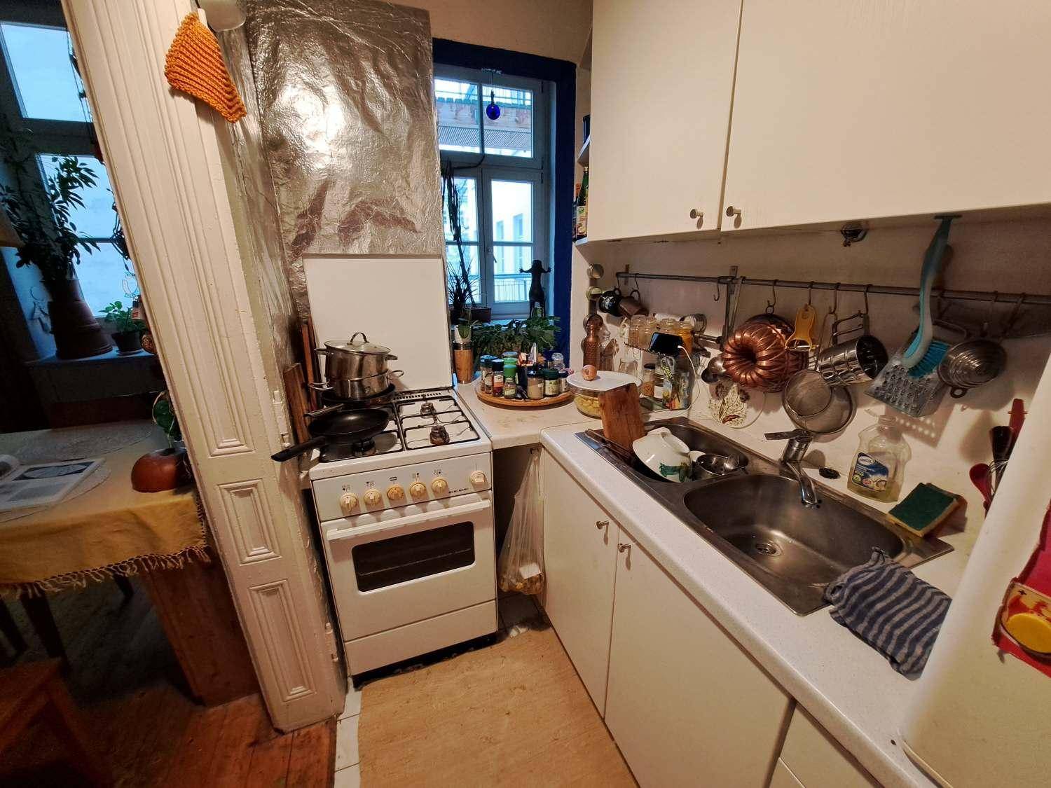 Kleine Küche mit weißer Einrichtung, Gasherd und Spüle, funktional und hell durch das Fenster.